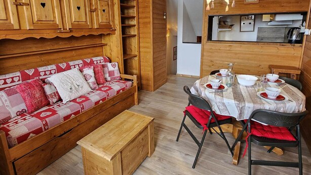 Una habitación acogedora con un sofá de madera, una mesa de comedor preparada para cuatro comensales y una zona de cocina.