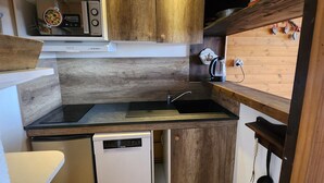 Cocina compacta con armarios de madera, microondas integrado, fregadero y lavavajillas.