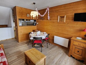 A cozy room with a wooden interior, a dining table set for four, a small kitchen area, and a television mounted on the wall. - Cozy triplex apartment - 4 guests (32m²) (Avoriaz)