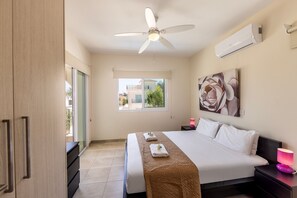Ein Hotelzimmer mit Bett, Deckenventilator, Klimaanlage, Fenster mit Blick und einem Bild an der Wand.