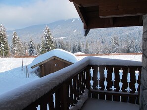 A wooden balcony with a snow-covered roof, a wooden fence, and a view of snow-covered trees and mountains in the background. - Spacious apartment with parking - 8 guests (Les Carroz d'Arâches)