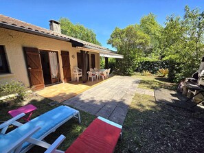 A patio with a table and chairs, a barbecue grill, and a pool area with lounge chairs. - Welcoming family house - 6 guests (Moliets-et-Maa)