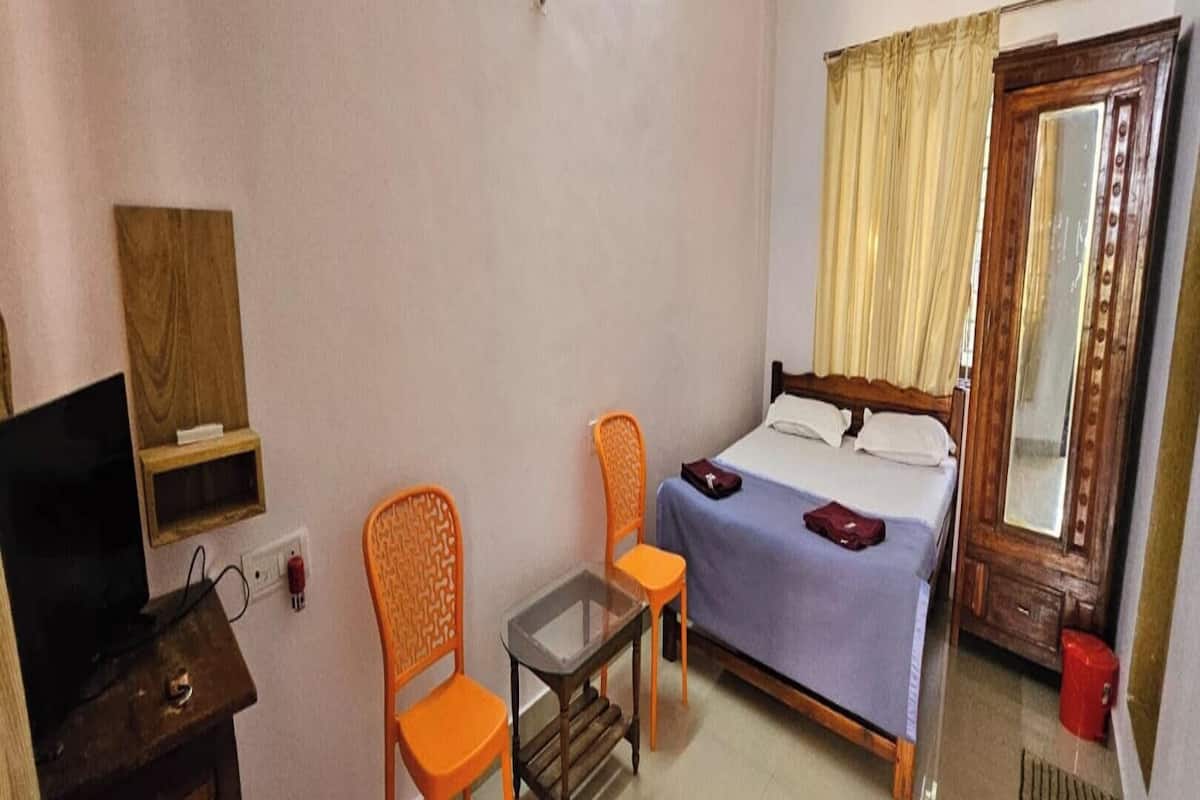 Un dormitorio con cama, dos sillas, una mesita, televisor y ventana con cortinas.