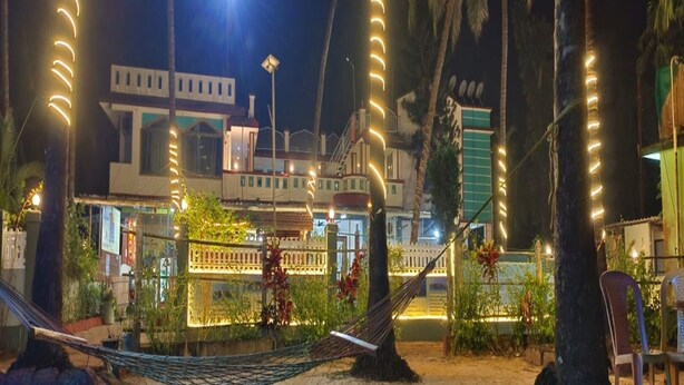 Un hotel frente a la playa con una hamaca, palmeras y un edificio con ventanas iluminadas.