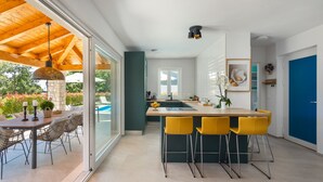 A modern kitchen with a central island, yellow bar stools, and a view of a pool. - Villa Norvegese by Villas Guide (Novigrad)