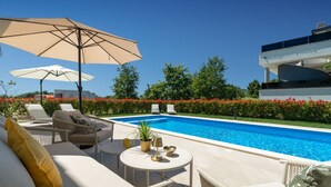 A pool area with lounge chairs, a table with a lamp, and a large umbrella. - Villa Norvegese by Villas Guide (Novigrad)