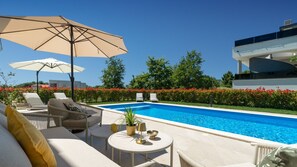 Ein Poolbereich mit Liegestühlen, einem Tisch mit Lampe und einem großen Sonnenschirm.