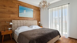 A bedroom with a wooden headboard, a large bed with white and dark bedding, a chandelier, a nightstand with a lamp, and a painting of a snowy landscape. - Villa Norvegese by Villas Guide (Novigrad)