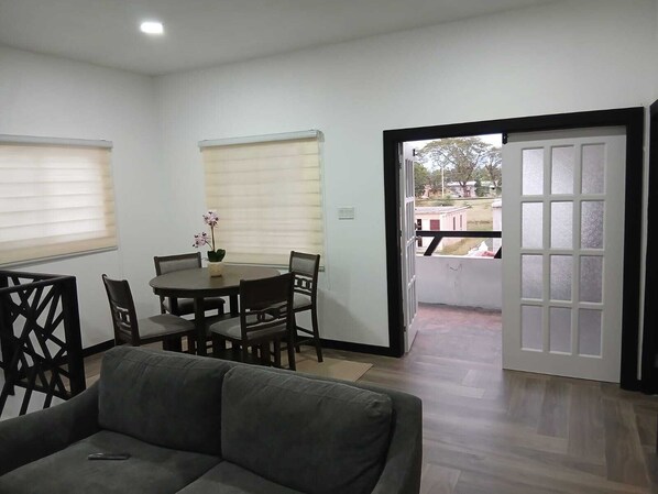A room with a dining table, chairs, a sofa, and a sliding glass door leading to an outdoor area.