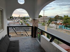 Varanda com sofá, vista para a rua e um prédio ao longe.