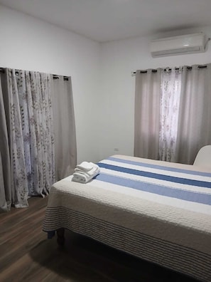 Ein Hotelzimmer mit Bett, Vorhängen, einer Klimaanlage und Holzboden.