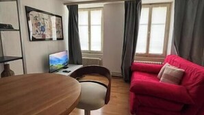 A room with a dining table, a red sofa, a TV, and a window with curtains.