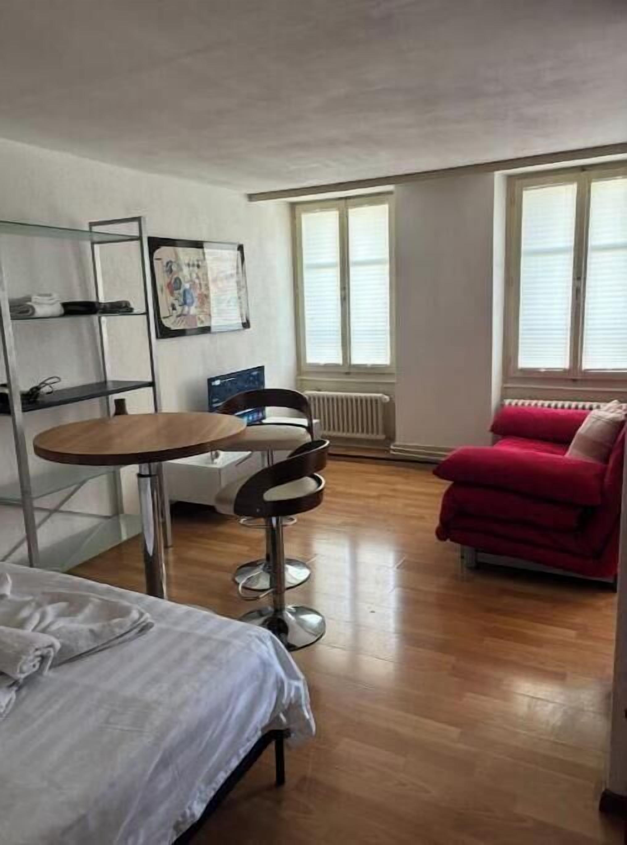 Ein Zimmer mit einem Bett, einem kleinen Tisch mit Stuhl, einem roten Sofa und einer Heizung.