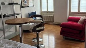 A room with a bed, a small table with a chair, a red sofa, and a radiator.