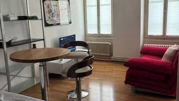 Ein Zimmer mit einem Bett, einem kleinen Tisch mit Stuhl, einem roten Sofa und einer Heizung.