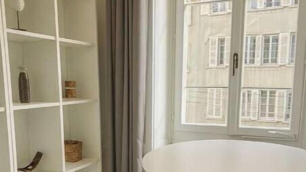 Ein Zimmer mit einem weißen Tisch, einer weißen Regaleinheit und Blick auf Gebäude durch ein Fenster.