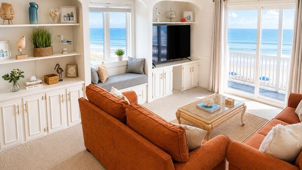 A living room with a sofa, a coffee table, a TV, and a view of the ocean.