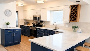 A modern kitchen with white cabinets, a large island, stainless steel appliances, and a clock on the wall.
