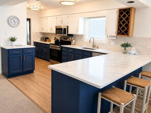 A modern kitchen with white cabinets, a large island, stainless steel appliances, and a clock on the wall.