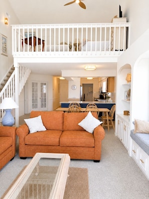 A spacious living area with a high ceiling, a dining table, and a kitchen in the background.