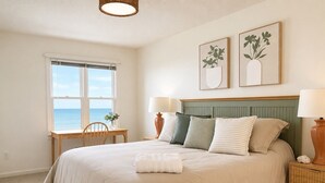 A bedroom with a bed, bedside tables, a window with a view, and two framed artworks on the wall.