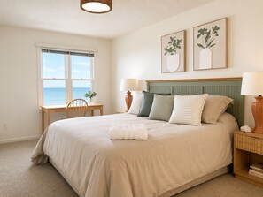 A bedroom with a bed, bedside tables, a window with a view, and two framed artworks on the wall.