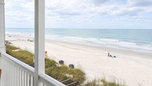 A beach view from a porch with a railing, a sandy beach, and the ocean.