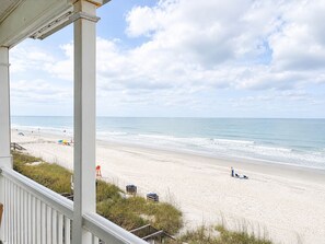 A beach view from a porch with a railing, a sandy beach, and the ocean.