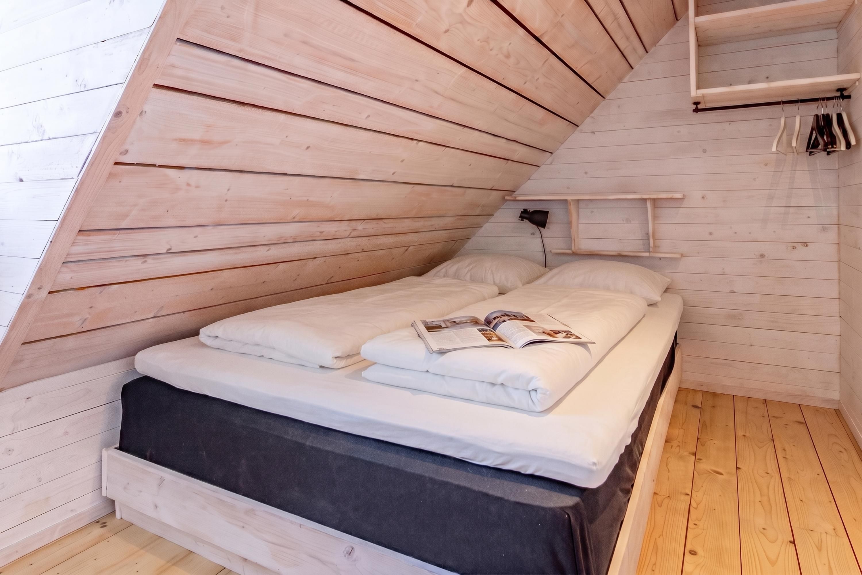 A bedroom with a sloped ceiling, a bed with white bedding, a black storage bench, and a small bedside table with a lamp.