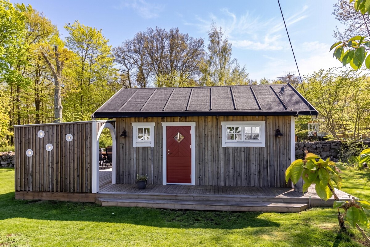A small wooden cabin with a red door, two windows, and a porch.