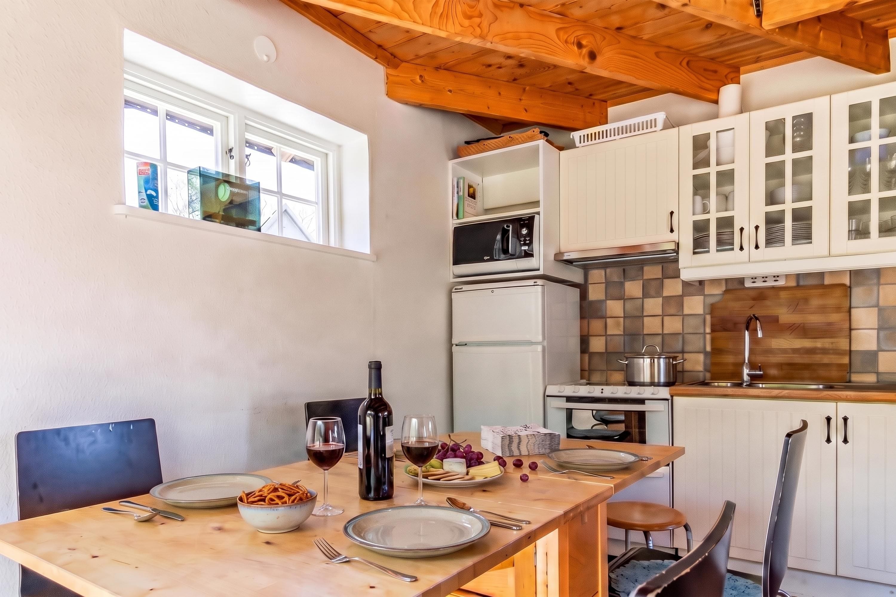 A dining area with a wooden table set for two, a wine bottle, and a bowl of snacks.