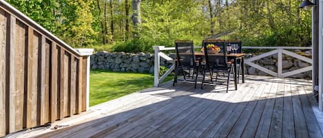 A wooden deck with a table and chairs, surrounded by a stone wall and lush greenery.