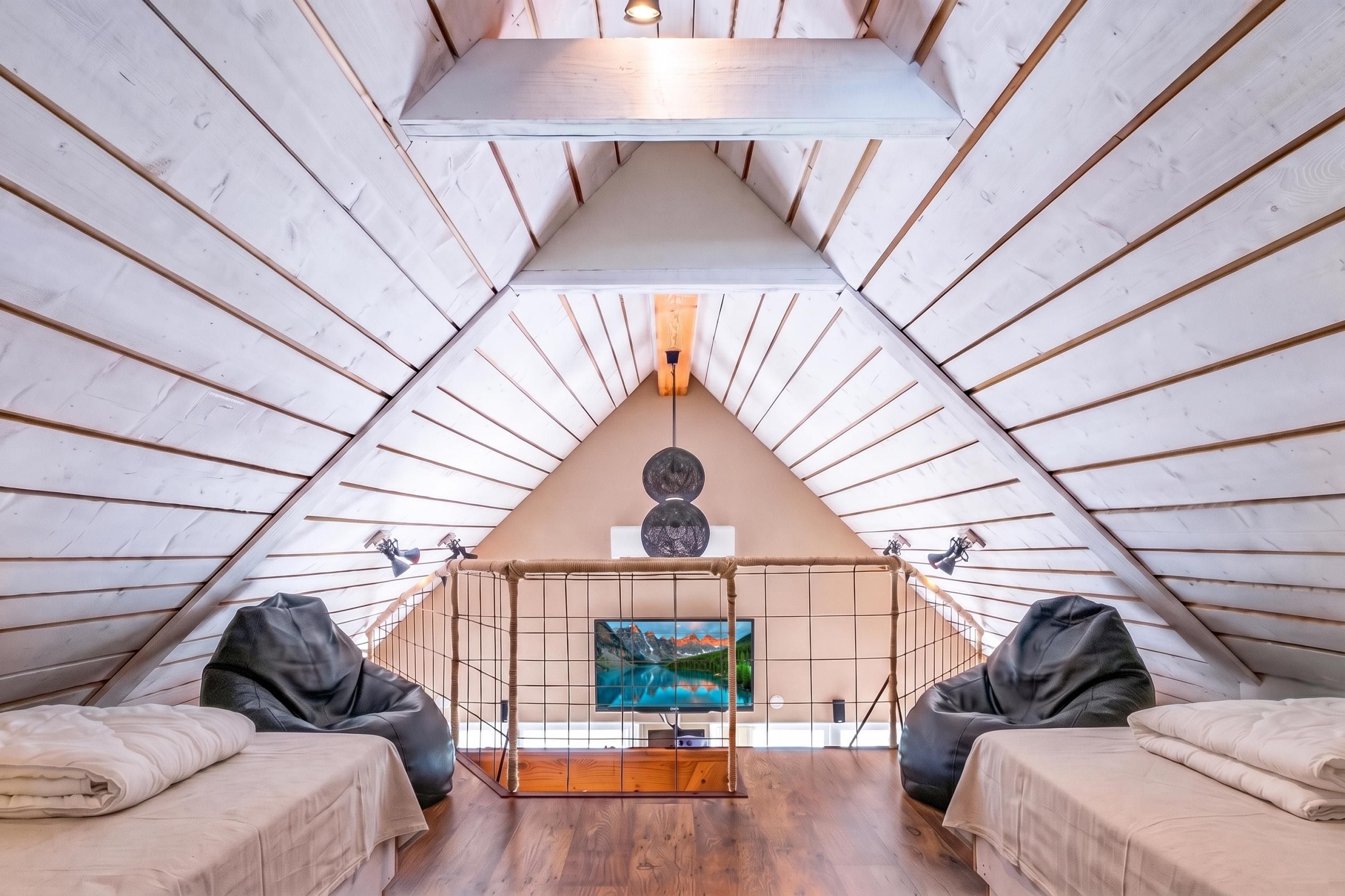 Un dormitorio acogedor en el ático, con techo inclinado, televisión y dos puffs.