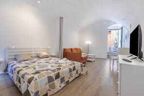 A modern hotel room with a bed, a sofa, a desk with a TV, and a lamp. - Palma Cabin Renovated Flat Old Town (Sanremo)
