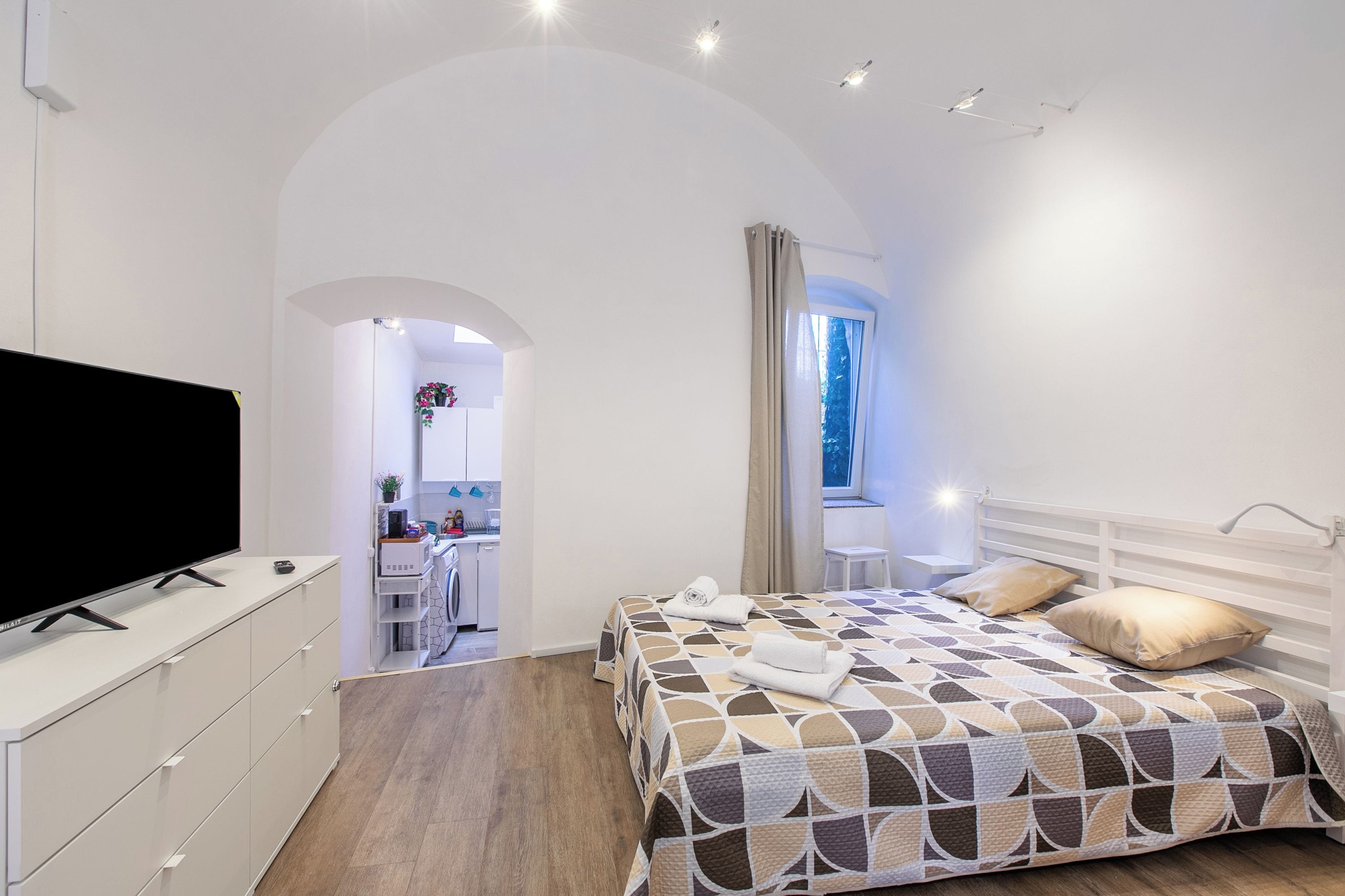 Um quarto com cama, televisão, escrivaninha e janela.