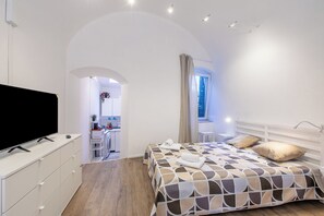 Um quarto com cama, televisão, escrivaninha e janela.
