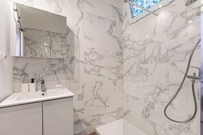 Casa de banho com parede de mármore, lavatório com produtos de higiene e chuveiro.