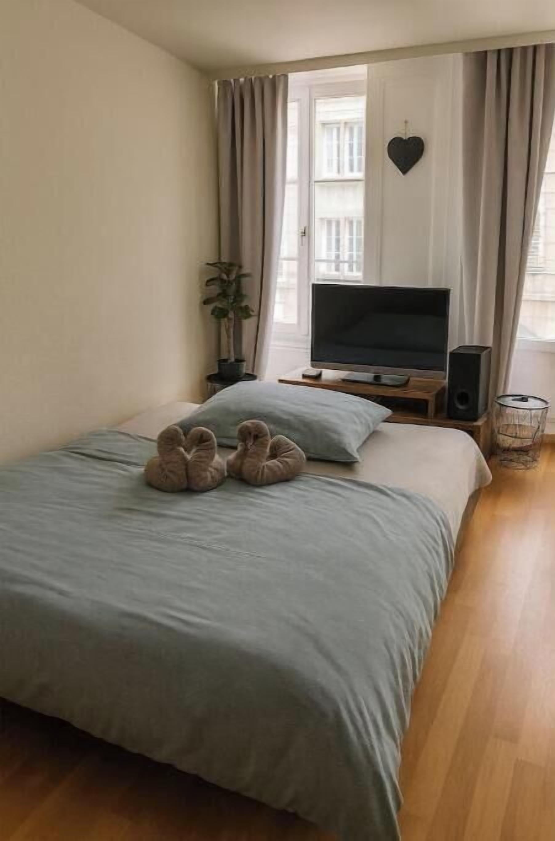 Ein Schlafzimmer mit einem Bett, einem Fernseher, einem Lautsprecher, einer herzförmigen Dekoration an der Wand und einem Fenster mit Vorhängen.