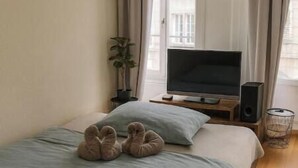 Ein Schlafzimmer mit einem Bett, einem Fernseher, einem Lautsprecher, einer herzförmigen Dekoration an der Wand und einem Fenster mit Vorhängen.