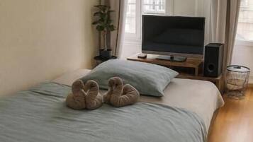 Ein Schlafzimmer mit einem Bett, einem Fernseher, einem Lautsprecher, einer herzförmigen Dekoration an der Wand und einem Fenster mit Vorhängen.