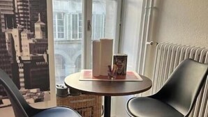 Ein Eckzimmer mit zwei schwarzen Stühlen, einem kleinen runden Tisch und Blick auf Gebäude durch ein Fenster.