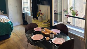 Un comedor con una mesa lista para dos, una ventana con vistas a edificios y un techo con vigas a la vista.