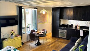 Una cocina moderna con armarios negros, un comedor con mesa y sillas, un televisor montado en la pared y suelo de madera.