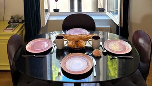 Una mesa de comedor dispuesta con platos, tazas y croissants, con vistas a un balcón y un mapa en la pared.