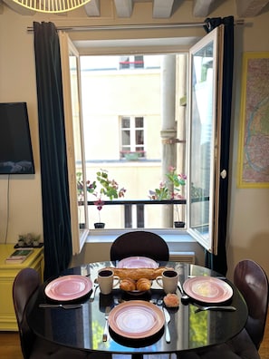 Ein Esstisch mit Tellern, Tassen und Croissants, mit Blick auf einen Balkon und einer Karte an der Wand.