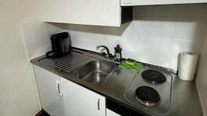 Een kleine keuken met witte kastjes, een roestvrijstalen spoelbak, een fornuis en een vaatwasser.