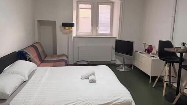 Een slaapkamer met een bed, bureau, stoel, televisie en raam.