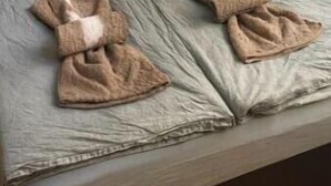 Ein Bett mit grauem Matratze, einem braunen Kopfkissen und zwei gefalteten Handtüchern.