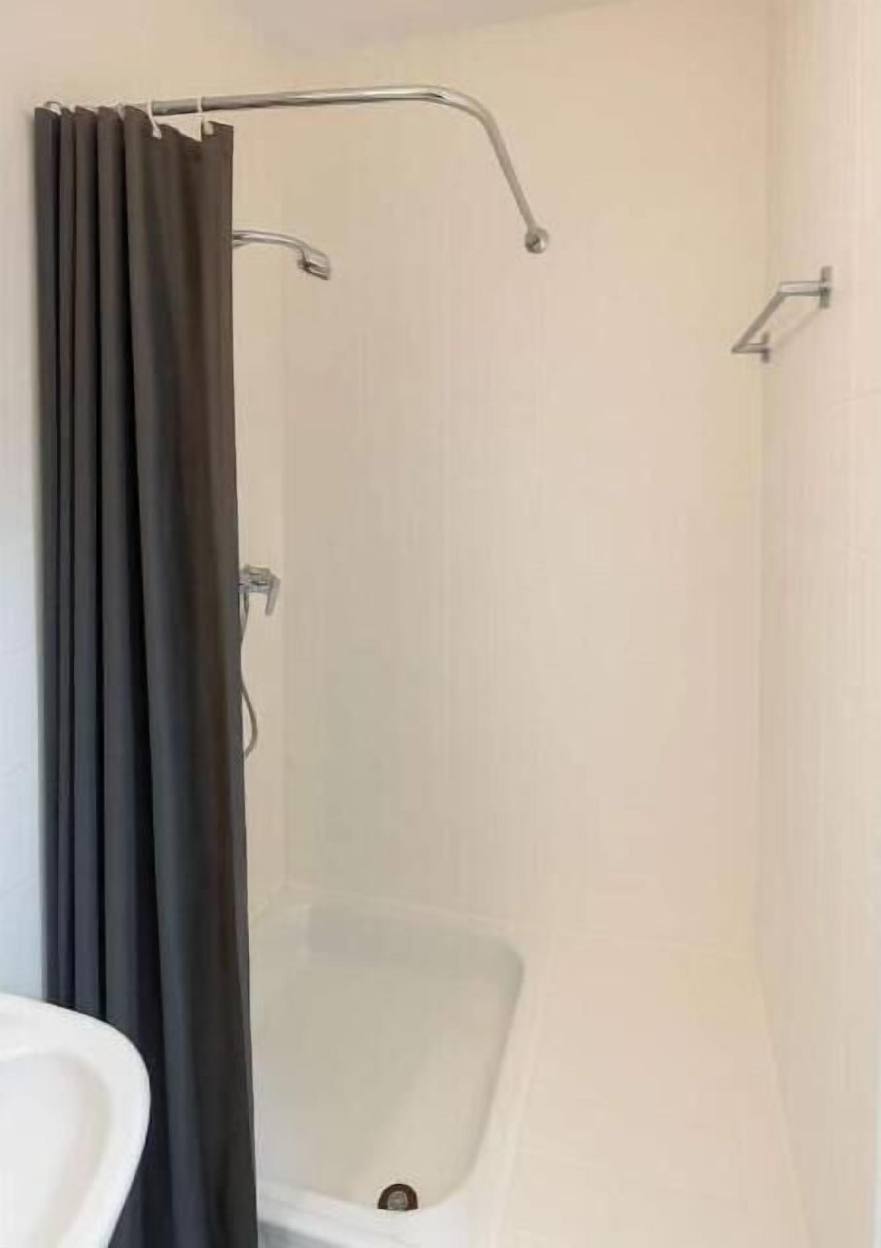 Eine Dusche mit Duschvorhang, eine Badewanne und eine weiße Wand.