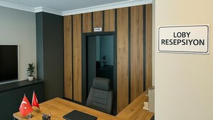 Un área de recepción con un escritorio de madera, una silla, un televisor y un cartel que indica la zona de recepción.